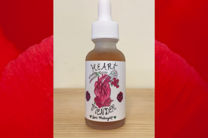 image of a tincture bottle on a wooden surface with the words "Heart Mender Dori Minight" and the image of a heart with plants coming from its ventricles. The background of the image is deep rose red.