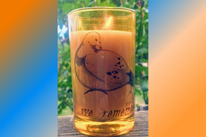 image of a lit candle in a glass with the decal "we remember" and the image of a dove, decorative blue and orange background